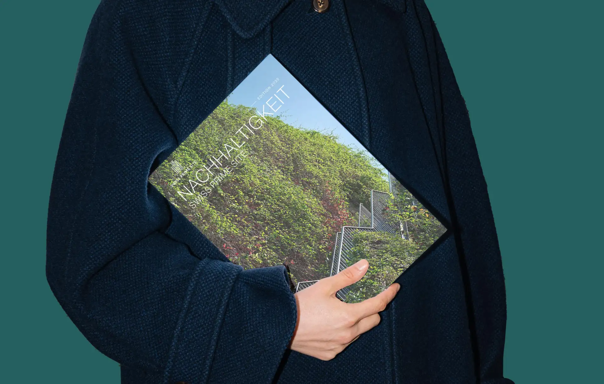 A person wearing a navy blue coat holds a magazine with a cover image showing lush green vines growing on a staircase. The scene conveys the theme of sustainability.